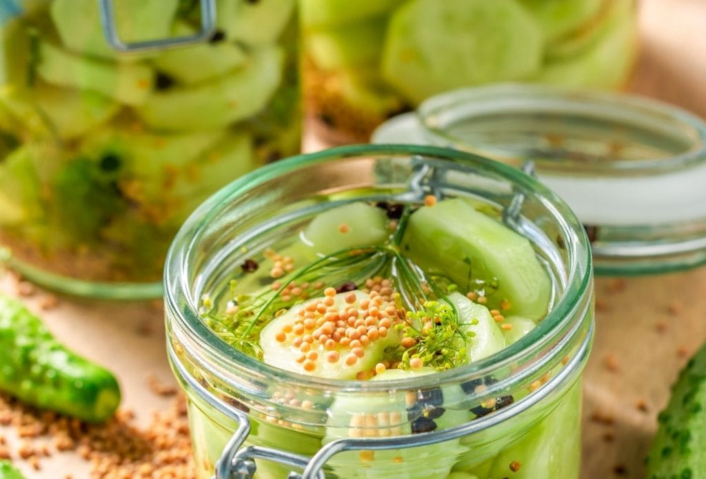 Cucumbers sliced and ready to pickle in a jar with spices on top