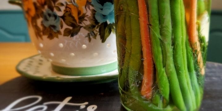 Spicy dilly beans in a jar on a board with a bowl on the table