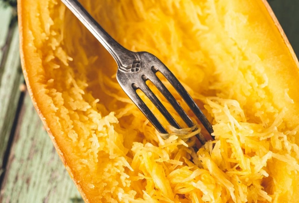 Cooked spaghetti squash half being scraped out with a fork