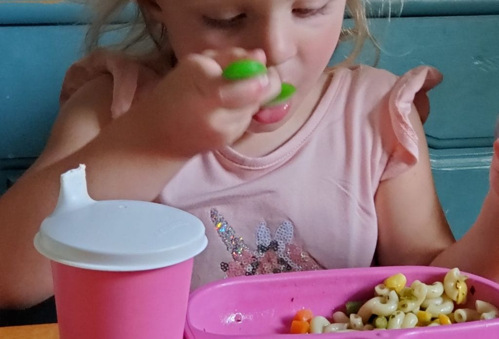child eating vegetable soup with a pink plate, green spoon and pink cup
