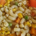 Vegetable noodle soup in a bowl with a red spoon