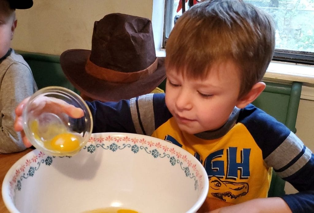 child pouring eggs into a mixing bowl for traditional pilgrim pumpkin pie