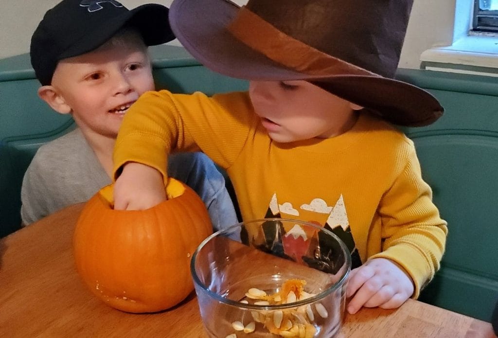 child digging pumpkin guts from a pumkin shell