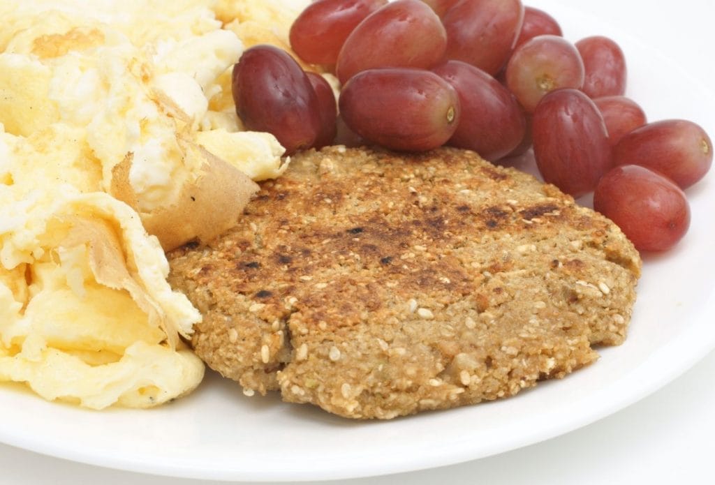 meatless monday breakfast with meatless sausage, grapes, and scrambled eggs on a plate
