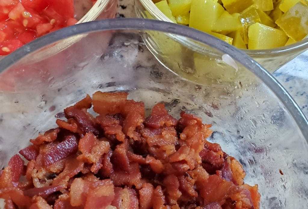bacon bits, pickle chunks, and tomato cubes toppings for keto bacon cheeseburger soup in clear glass bowls on the counter