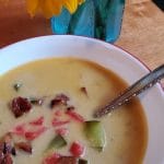 keto bacon cheeseburger soup in a bowl with a spoon on the table by some flowers