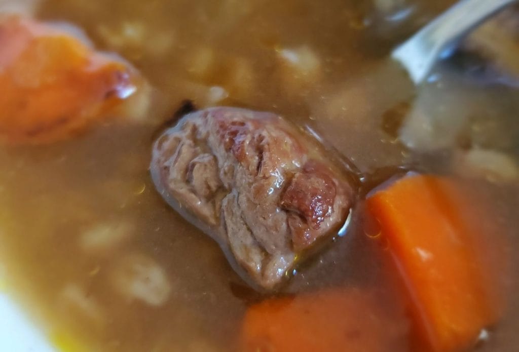 beef, vegetable, and farro soup in a bowl with a big piece of beef on top