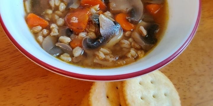 Beef, vegetable, and farro soup in a bowl on the table by some crackers