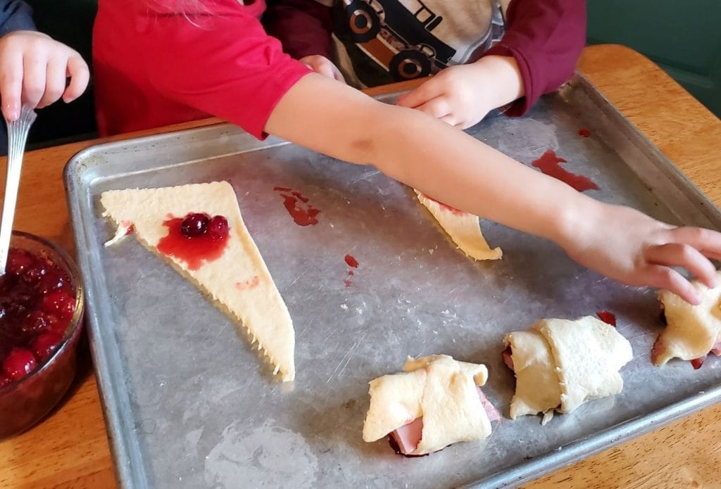 rolling ham and cranberry sauce in crescent roll dough