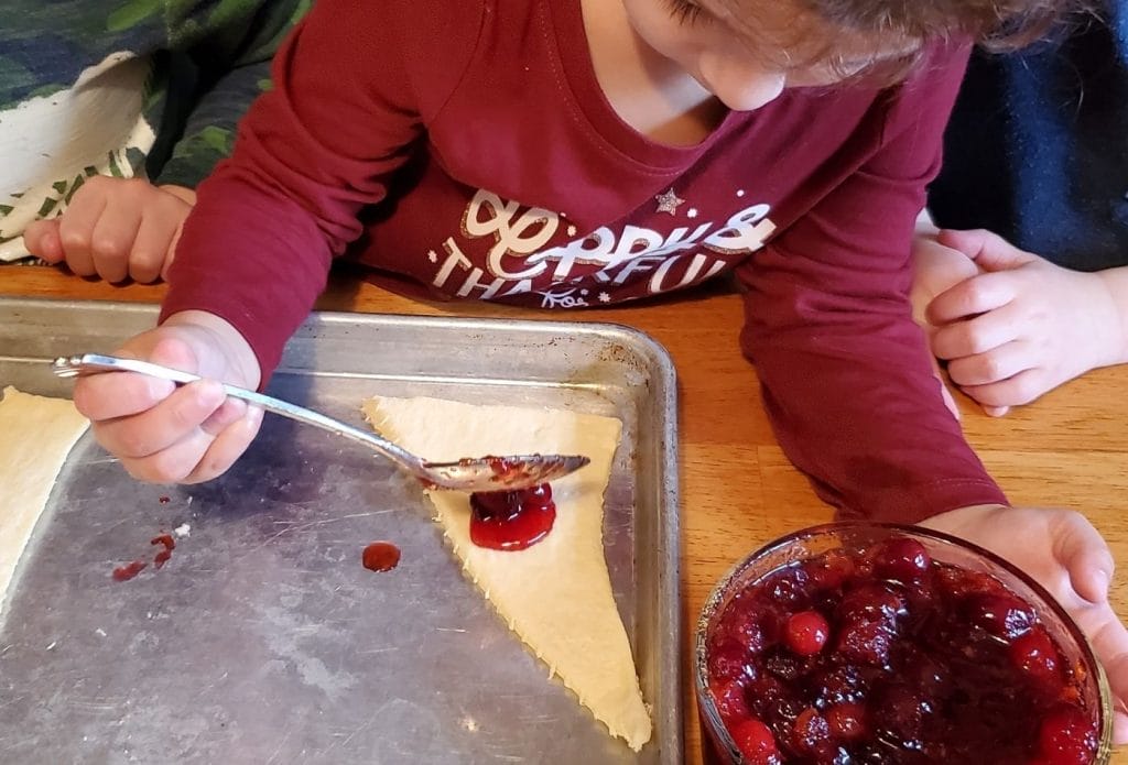 child spooning cranberry sauce onto a croissant for a roll up