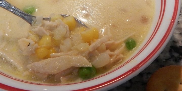 A bowl of soup ideas for dinner with peas, corn, chicken scooped up on a spoon in a bowl