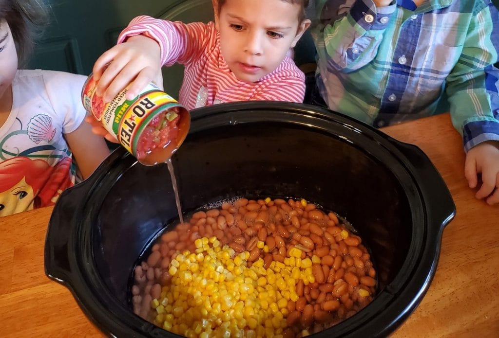 kids making taco soup in a crock pot, pouring in cans of ingredients