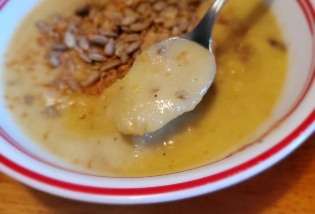 Spoon of roasted summer squash soup above the bowl