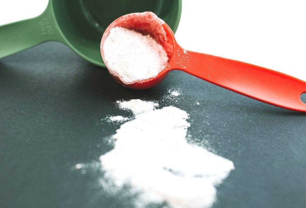baking soda measured in a measuring spoon next to a measuring cup on a table.