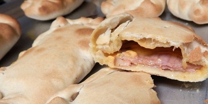 ham and cheese hot pockets on a sheet pan, one is cut in half so you can see the gooey inside