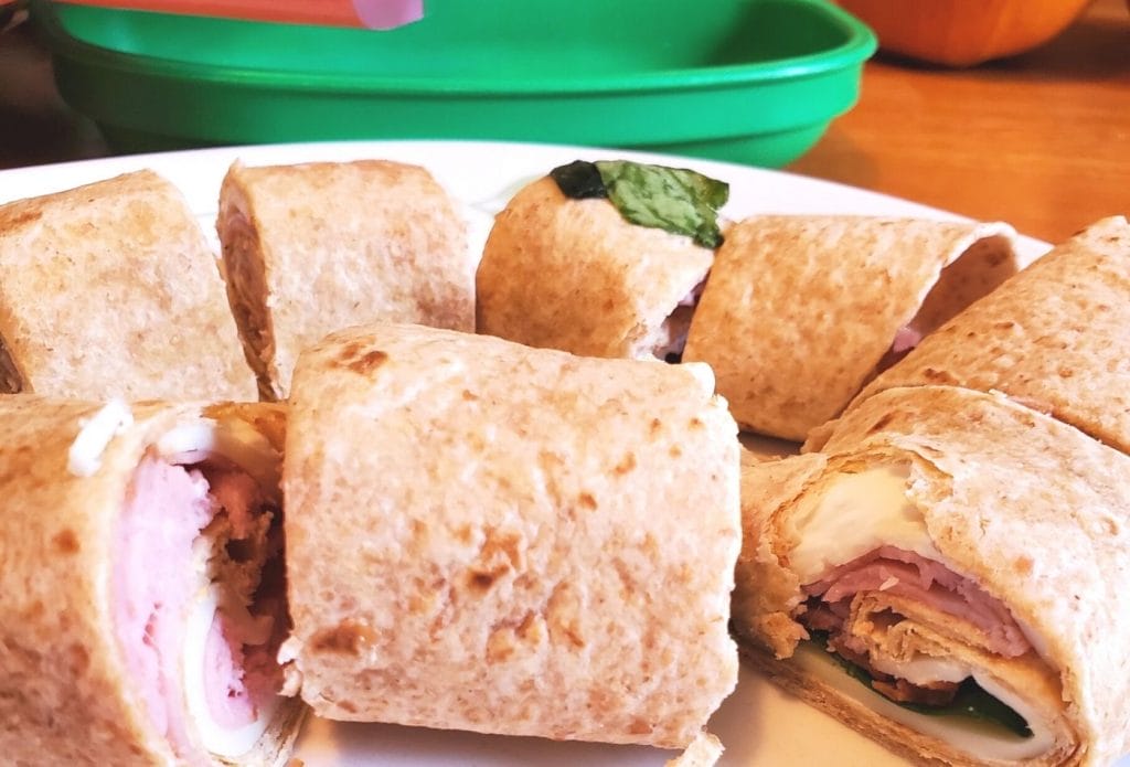 rolled tortilla pinwheels with spinach, lunch meat and cheese on a plate with the daycare lunch plates