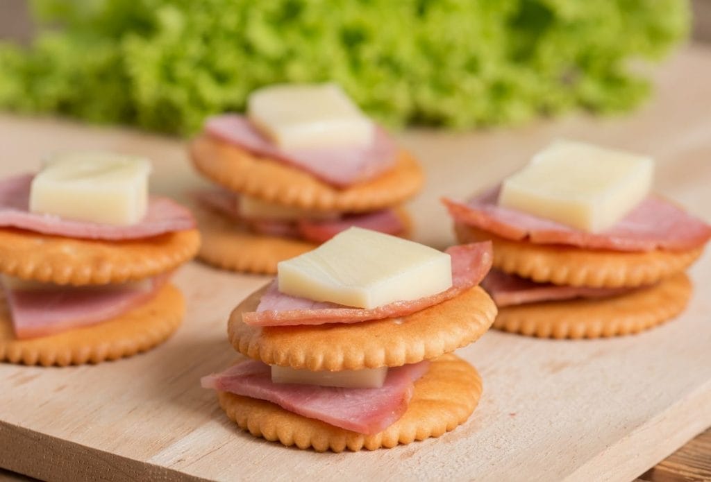 crackers with meat and cheese stacked on top on a board