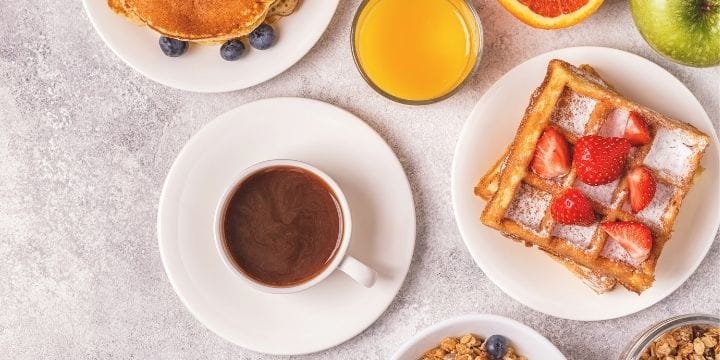 coffee, orange juice, pancakes, waffles, granola on a table with fruit