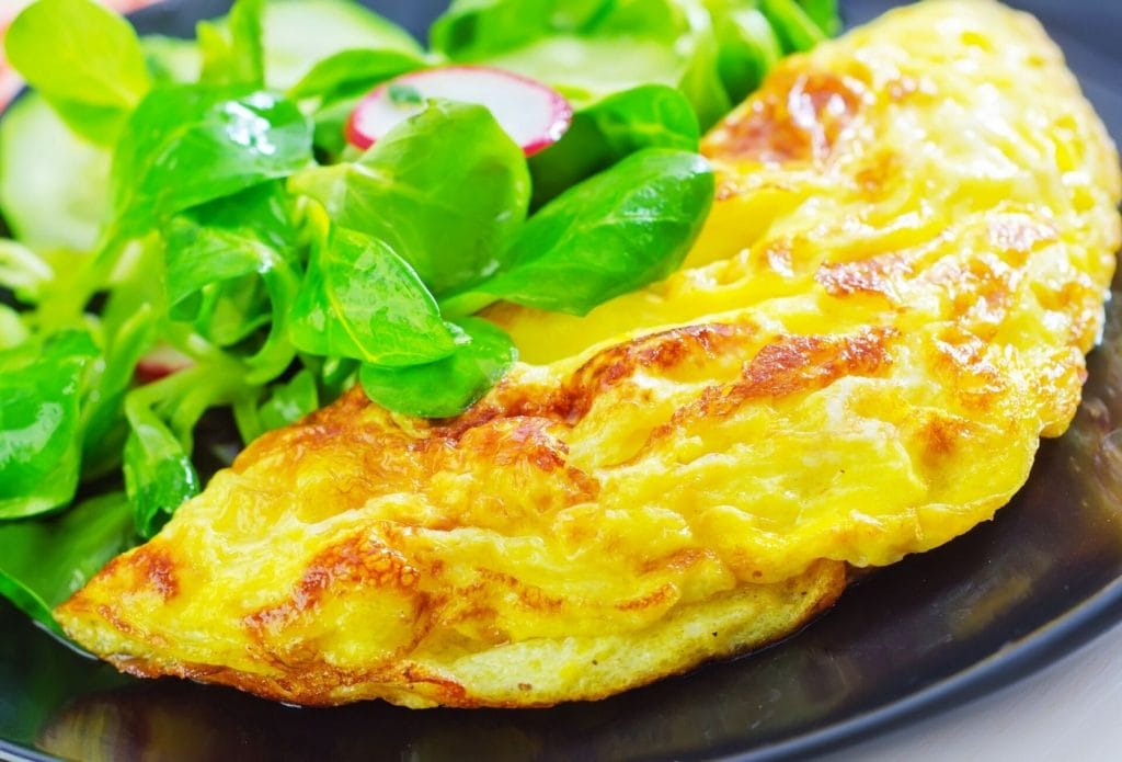 beautiful omelette on a plate with a green salad with thinly sliced radishes
