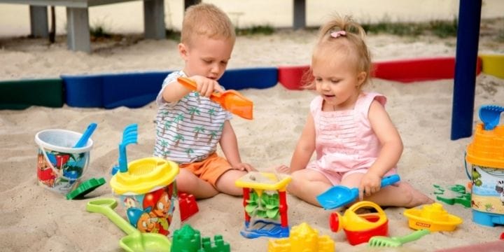 two kids playing in a sand box with digging toys at daycare