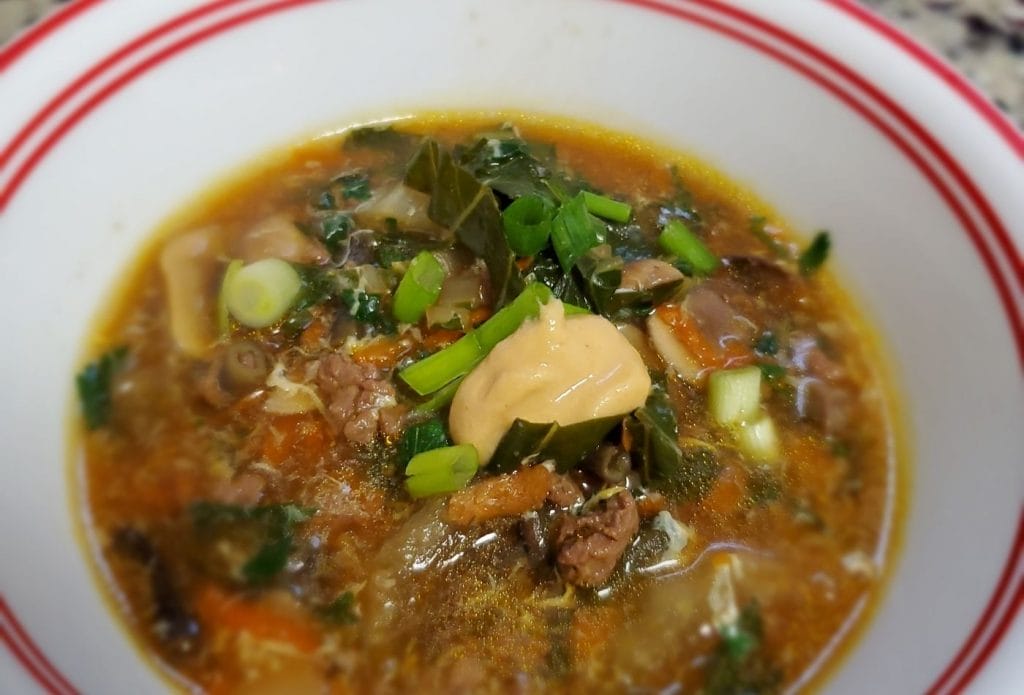 chinese inspired beef soup with vegetables and spicy mustard on top