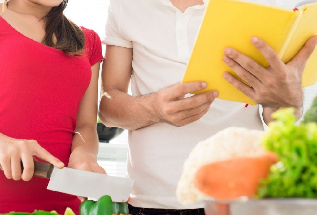 two people cutting up veggies and reading a book for beginning cooking instructions