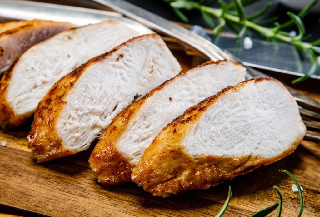 sliced air fryer chicken breast fanned out on a cutting board with herbs and a spoon nearby