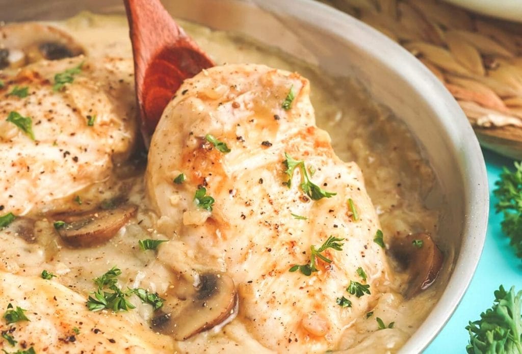 creamy champagne chicken in a pot with a spoon lifting up a chicken breast out of the sauce