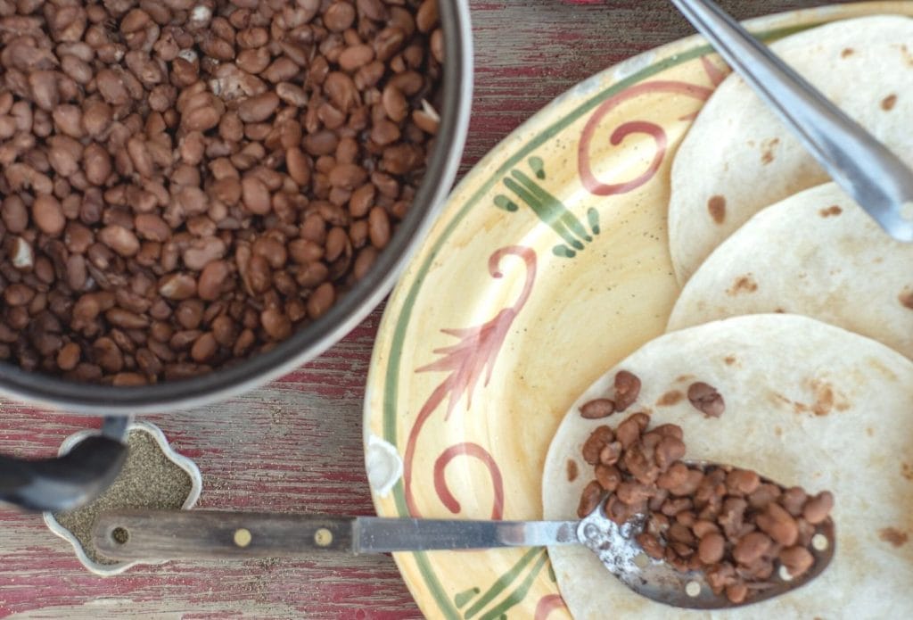 pot of beans and plate of tortillas with a spoon full of beans going on
