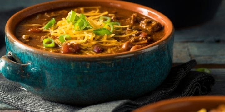 rotel chili in a blue bowl on a grey towel topped with cheese and green onions