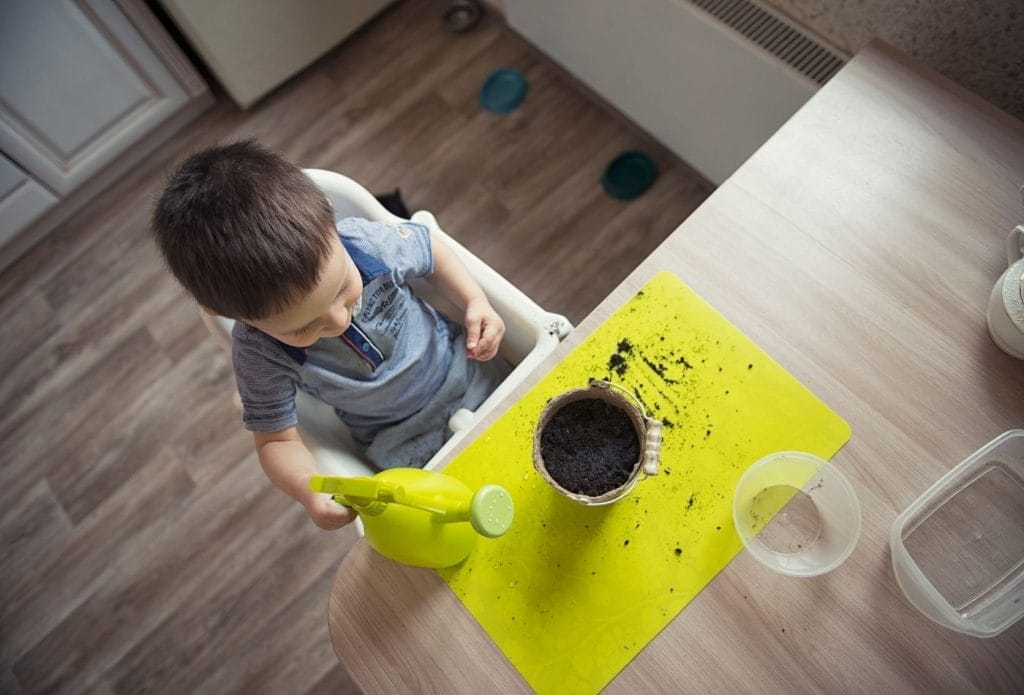 toddler planting seeds for a garden activity at a table with a pot and a watering can