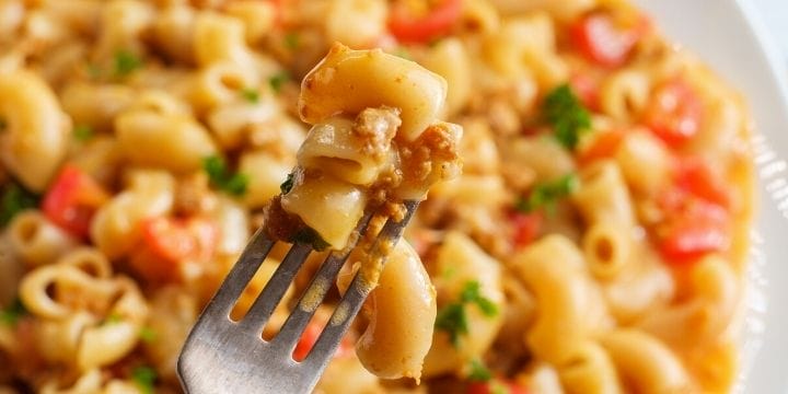 cheese and ground beef pasta with vegetables on a plate with one bite on a fork