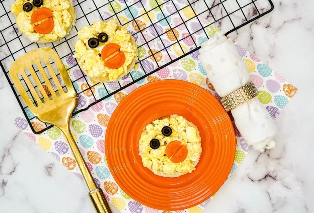 easter chick toast on a plate with silverware and a gold spatula and a tray full of easter chick toast nearby