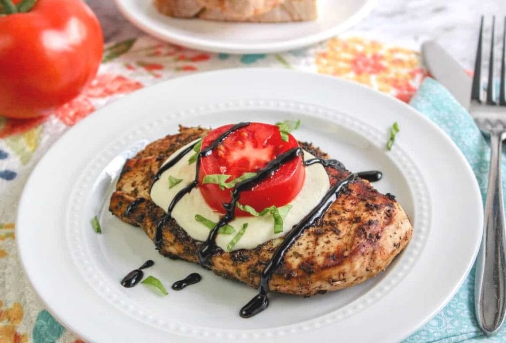 grilled bruschetta chicken on a plate with melted mozzarella and a slice of tomato on top
