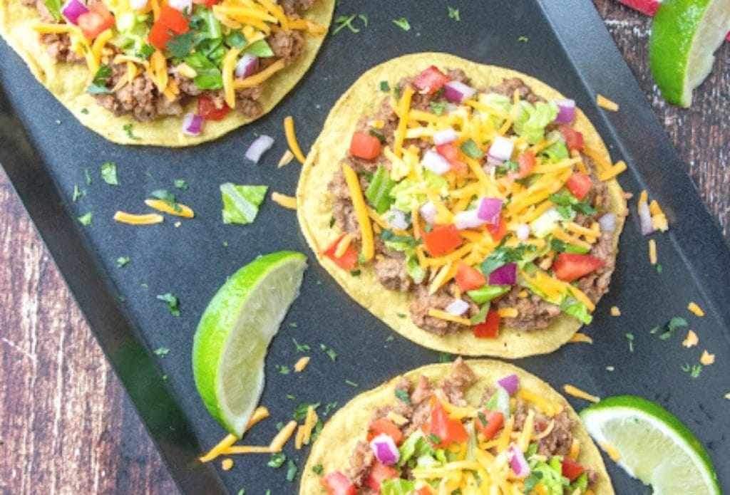 ground beef and refried bean tostadas on a tray with wedges of lime