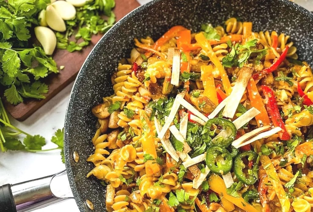 honey chipotle chicken pasta in a skillet next to a cutting board. Hot peppers and garnish on top