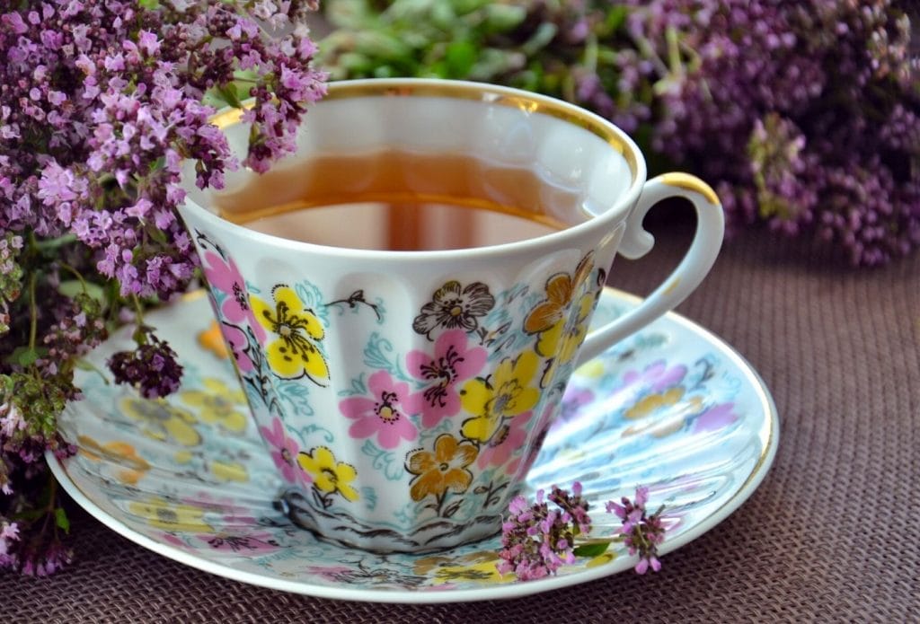 cup of marjoram tea on a table with marjoram blooms