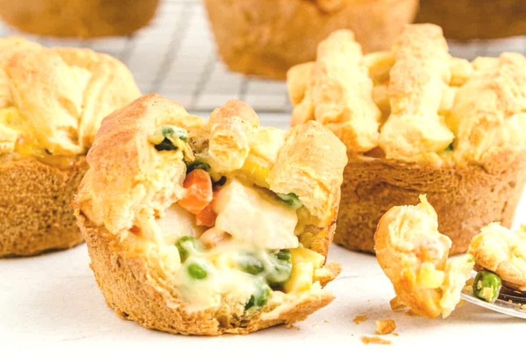little mini chicken pot pies on a cooling rack, one is spilled open showing the filling
