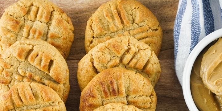 ninja foodi air fryer peanut butter cookies lined up on a board with a bowl of peanut butter and a blue striped towel