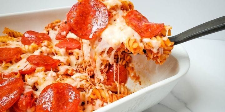 pepperoni pizza pasta bake in a casserole dish with a piece lifted up