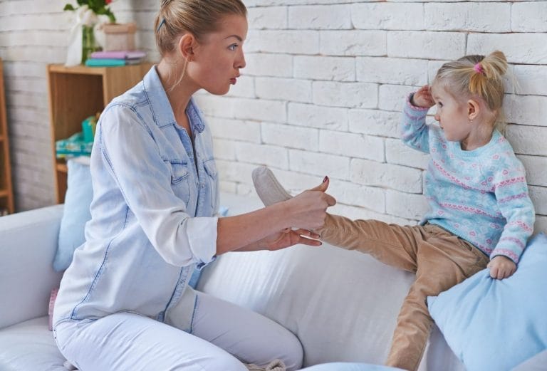 childcare provider putting a sock on a daycare child on the couch