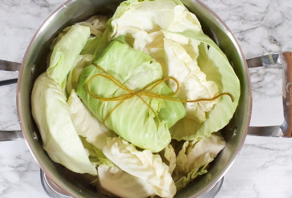 pot of cabbage leaves with bacon and spice bundle on top