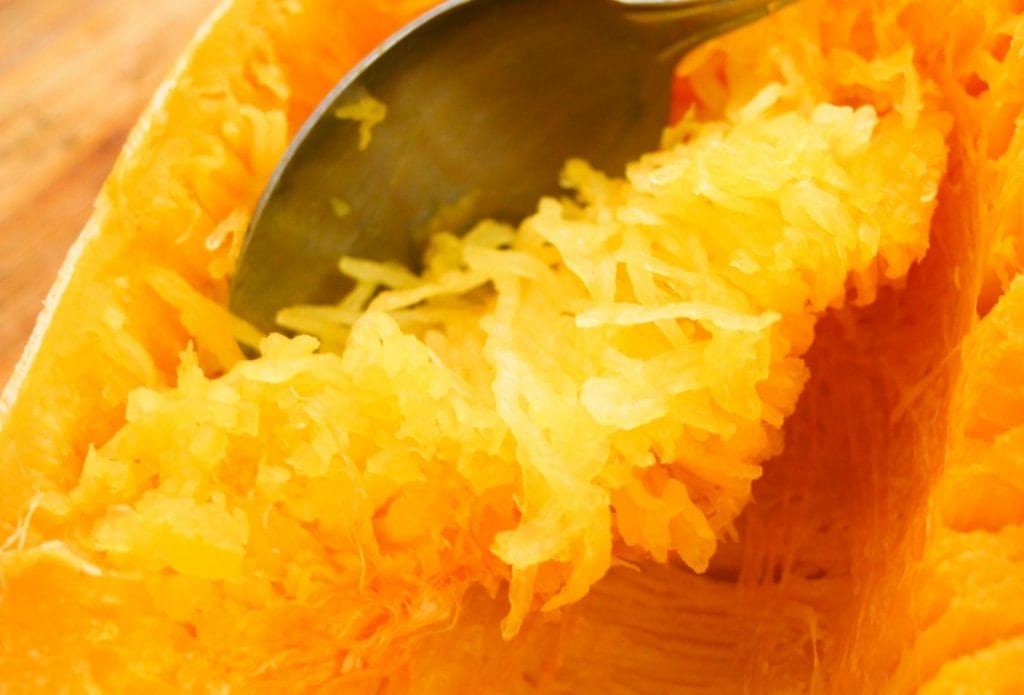 spaghetti squash being scraped out of the shell with a spoon.