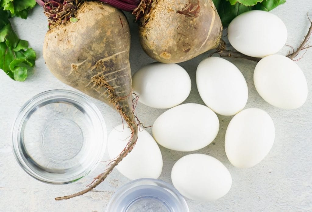 white eggs, raw beets with tops, and bowls of clear liquid on the table
