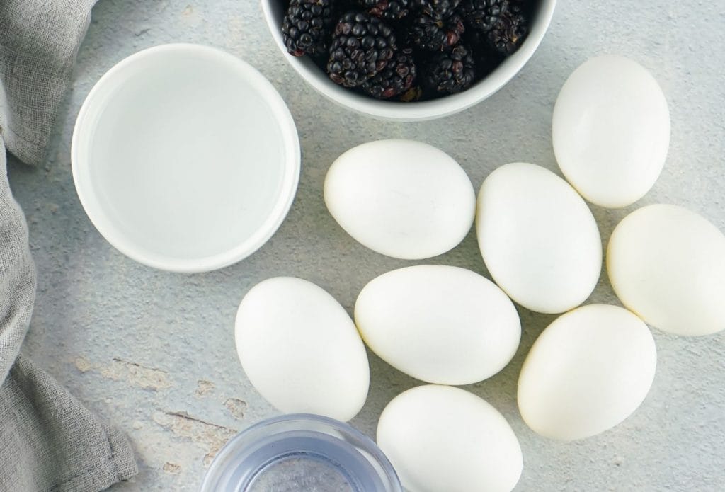 white eggs with a bowl of blackberries and two bowls of clear liquid on a tablbe