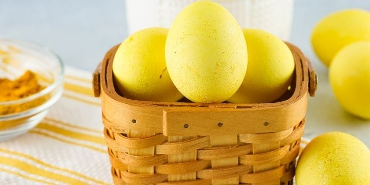 easter eggs dyed with turmeric in a basket with a bowl of turmeric, a spice jar and more yellow eggs around it