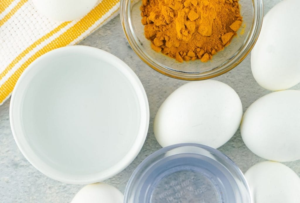 white eggs with clear liquid in bowls and turmeric and a yellow dish towel