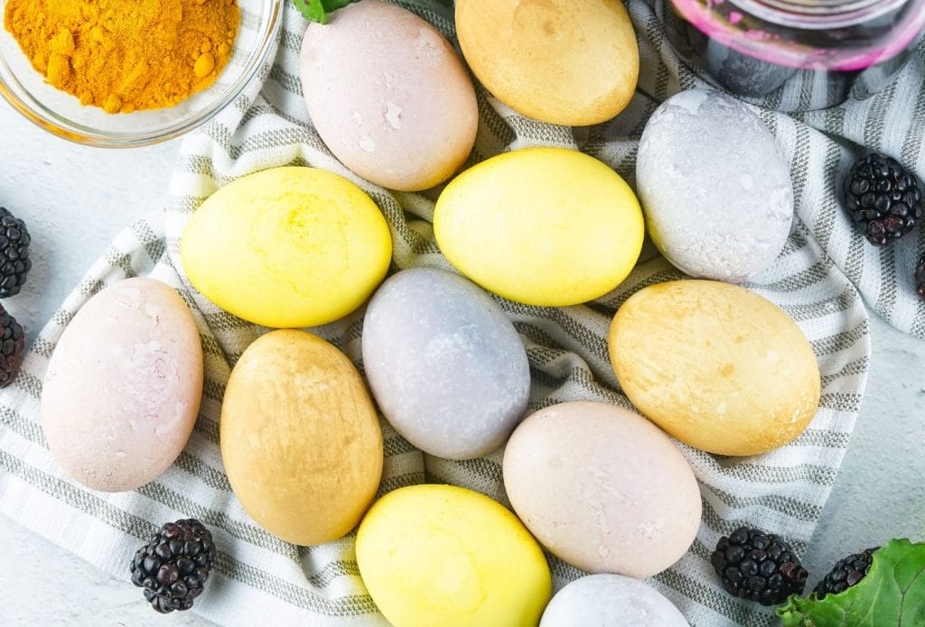 multi colored naturally dyed eggs on a towel with turmeric, blackberries and more