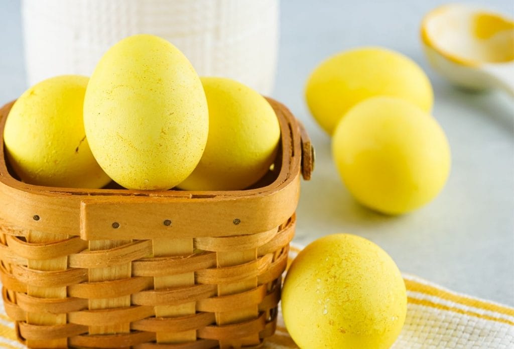 yellow dyed eggs in a basket with some on the table and a spice jar