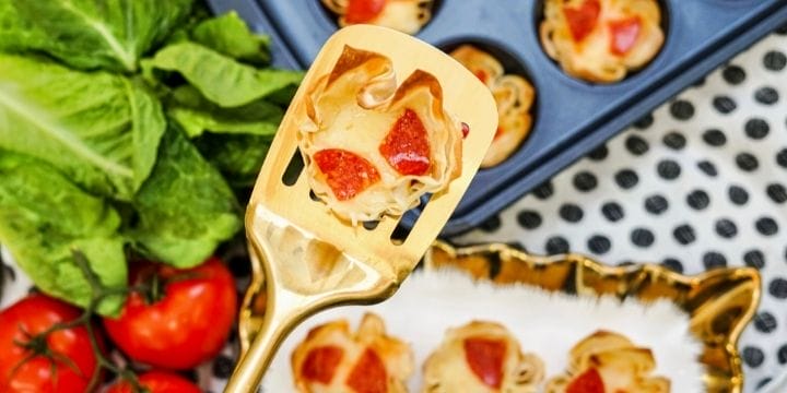 pepperoni pizza cup on a spatula above a plate of cups, a muffin tin of cups and some lettuce and tomatoes